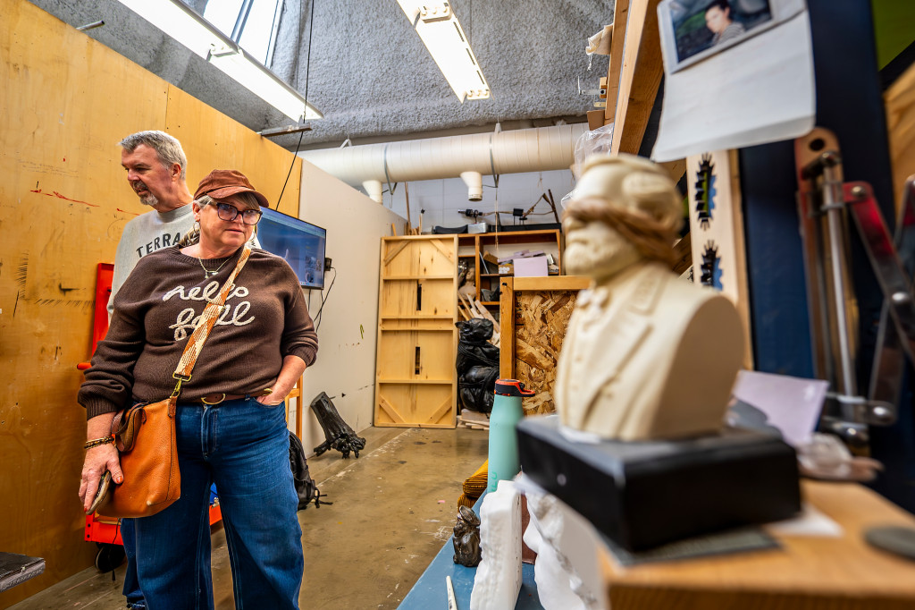 People walk through an room filled with sculptures and paintings.