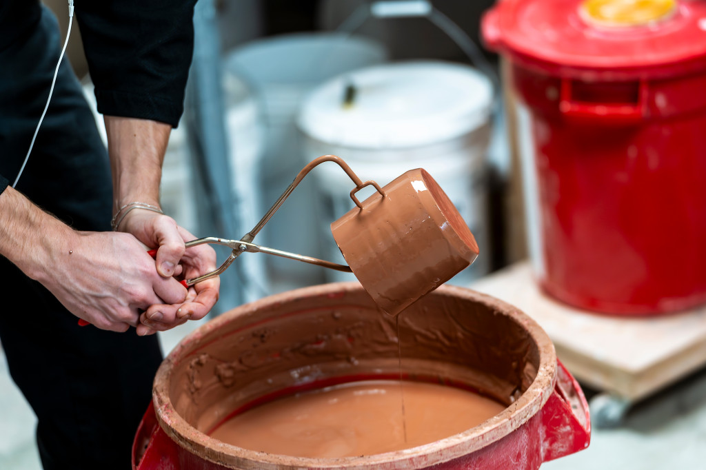 A hand holds tongs that lift a piece of pottery out of a kiln.