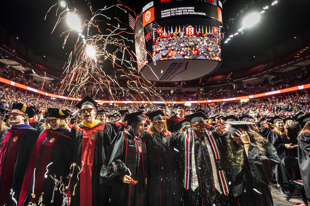 Streamers fall from the ceiling inside the Kohl Center as graduates in commencement robes smiles and dance.