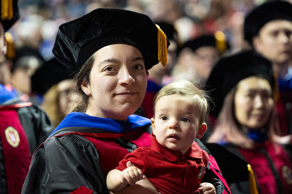 A woman in an academic robe holds a little baby.