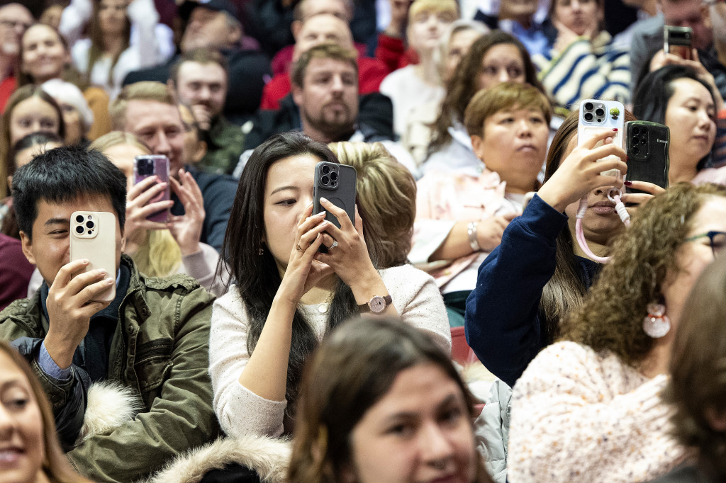 People in the audience take cell phone photos and cheer.