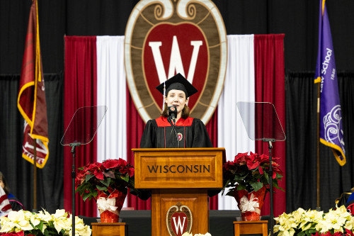 A woman speaks at a podium, a large W crest is behind her.