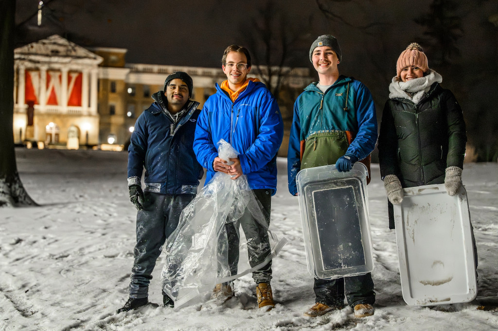 Four students hold stand on a snowy hill holding sledding gear.