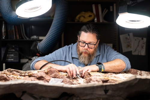 A man works carefully with some fossils on a table.