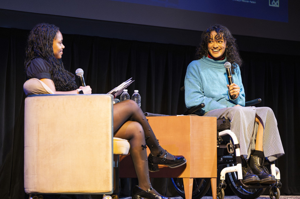 Two women sit on stage chatting.