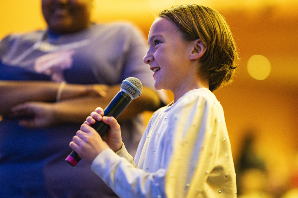 A girl holds a microphone and speaks into it from the audience.