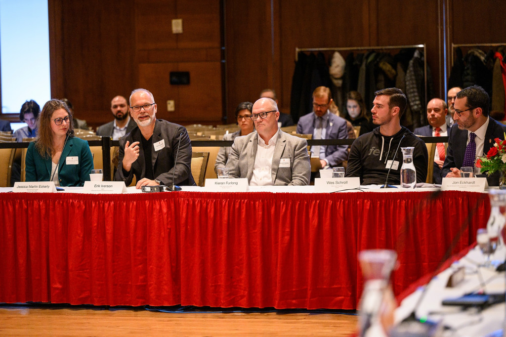 Five people sit at a table with microphones, and one of them speaks.