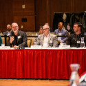 Five people sit at a table with microphones, and one of them speaks.