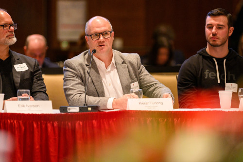 A man sitting at a table on a panel speaks into a microphone.