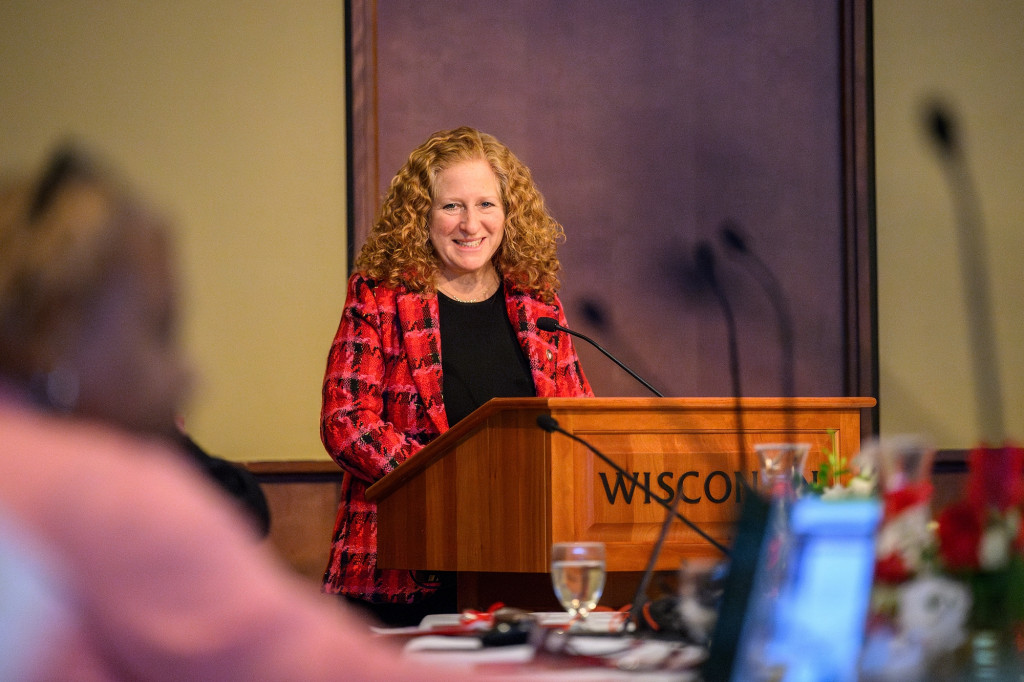 A woman standing at a podium speaks and smiles.