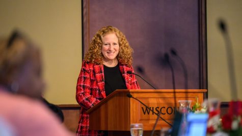 A woman standing at a podium speaks and smiles.