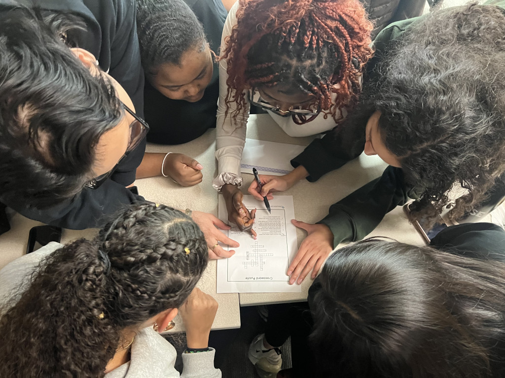 A circle of heads hunch over a paper as the group works to solve a clue presented during the scavenger hunt.