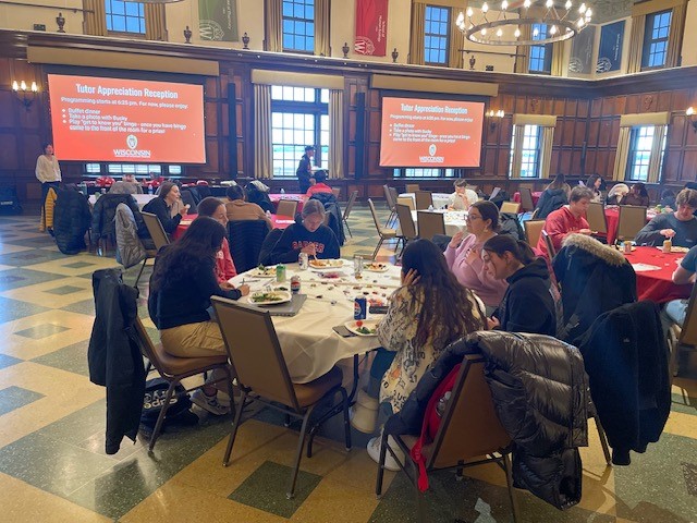 A group of people sit around tables in a banquet hall.