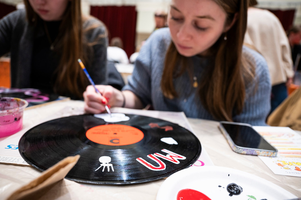 A student paints a red "UW" logo on a vinyl record.