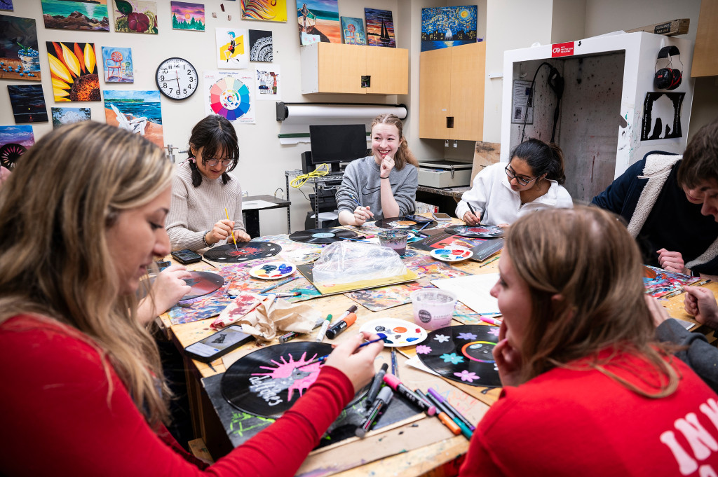 Students sit around a table painting records and talking.