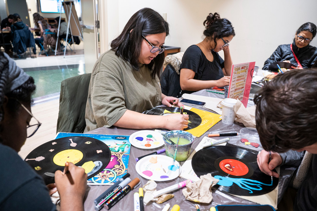 Students sit around a table painting on vinyl records.