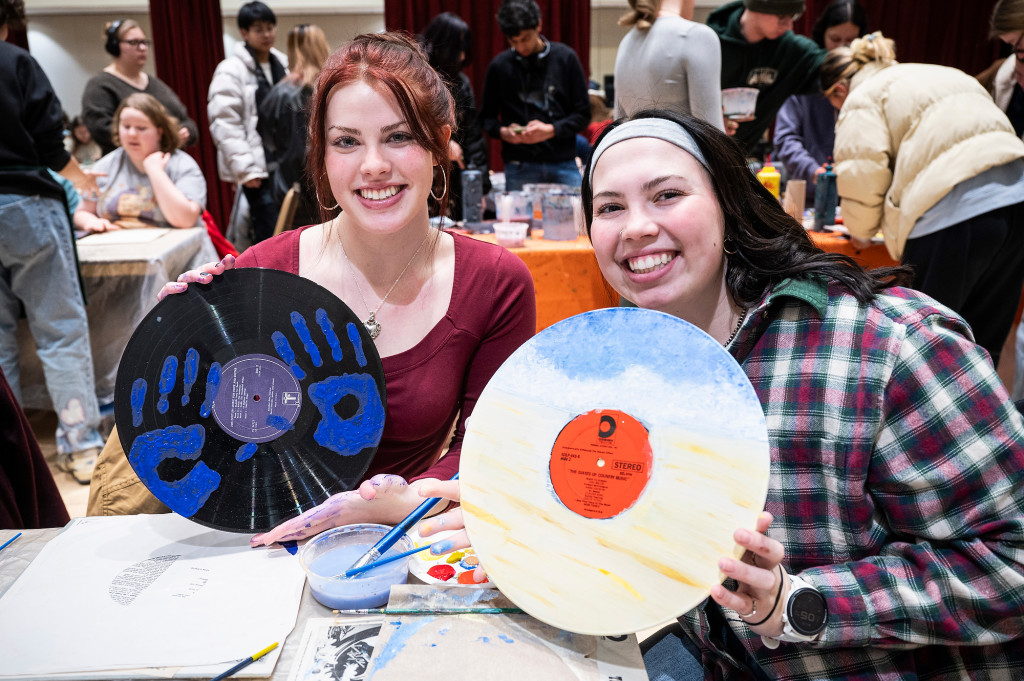 Two women hold up vinyl records that they painted.