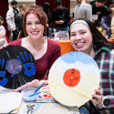 Two women hold up vinyl records that they painted.