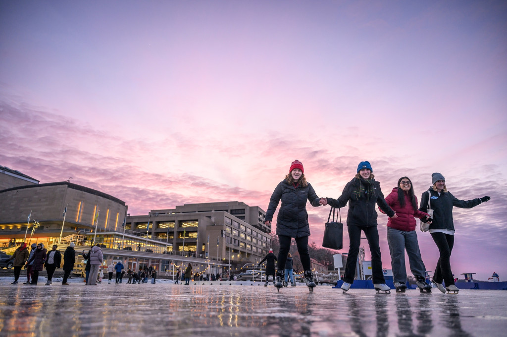 Photo of several people walking on an iced over lake with a colorful sunset behind tehm.