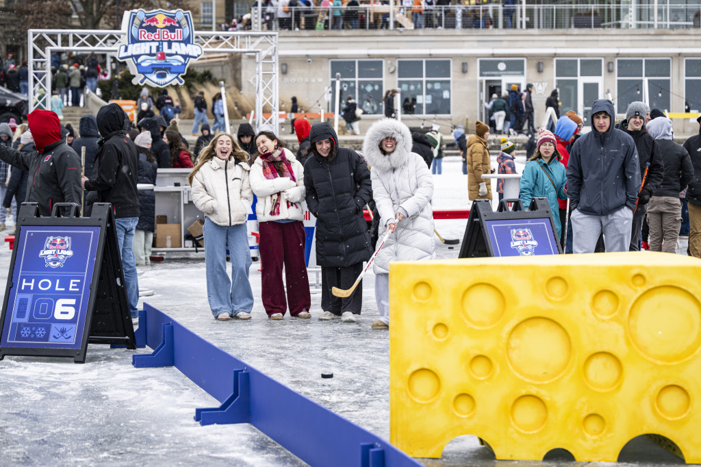 Students stand on the ice, one holding a hockey stick, ready to hit a ball down an icy lane toward a target.