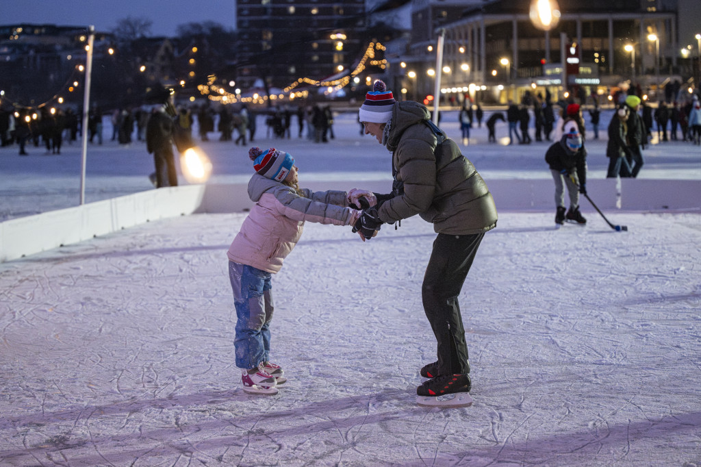 A woman and a young girl hold hands as they skate on a lake.