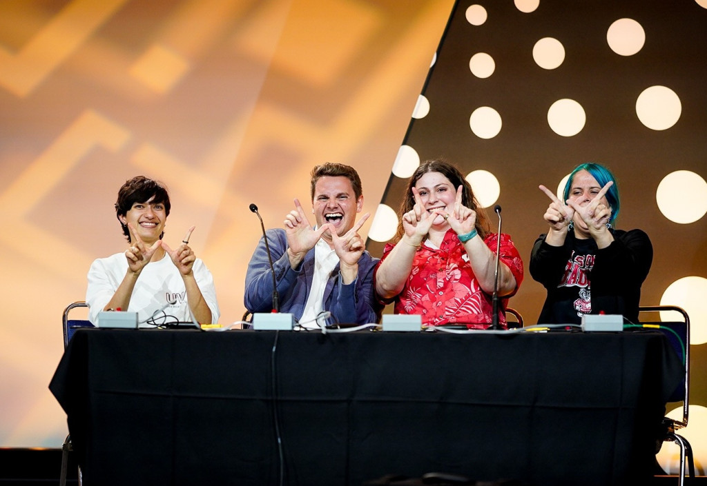 Four people flash W signals and smile on a stage.