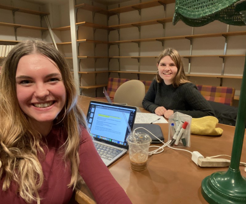 Two women sit on opposite sides of a table, smiling at the camera.