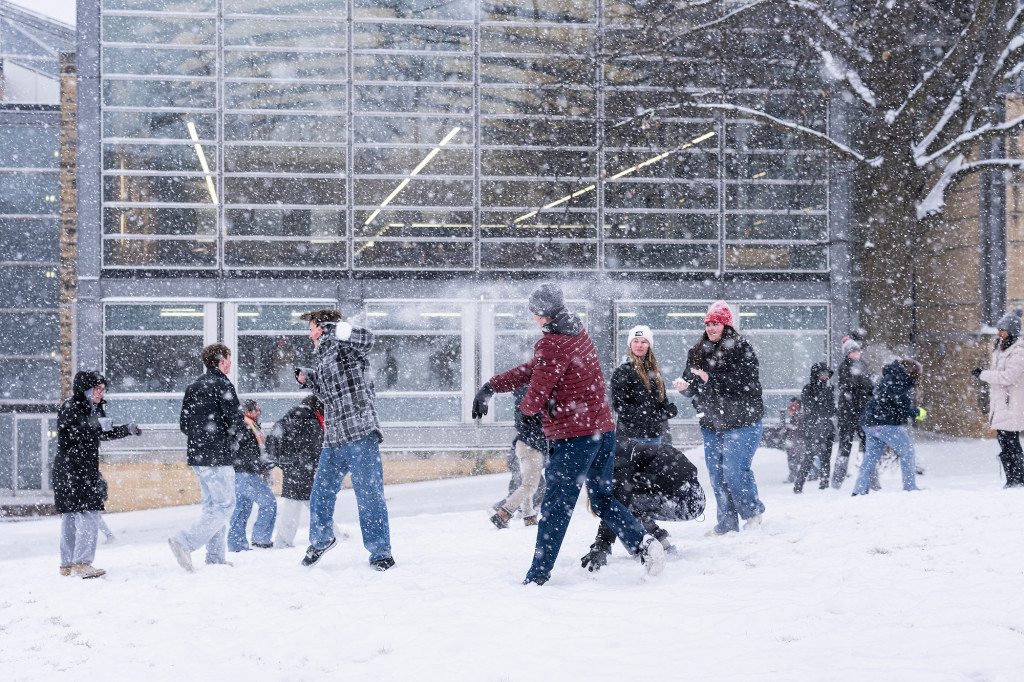 A group of students throw snowballs at each other outside of the Law Library on Bascom Hill. Students are bundled up in winder gear while also wearing smiles on their faces.