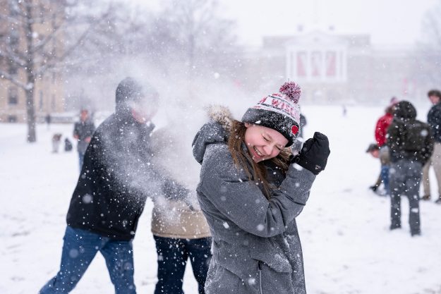 A student laughs as she shields her face from an incoming snowball during a snowball fight on Bascom Hill.