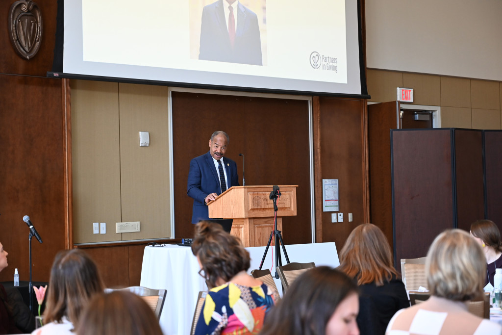 A man stands at a podium and speaks to a room full of people.