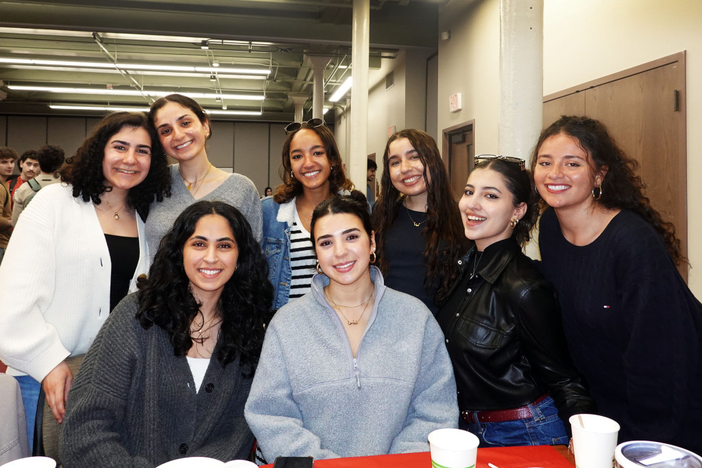 A group of students stand or sit behind a table and pose for the camera.