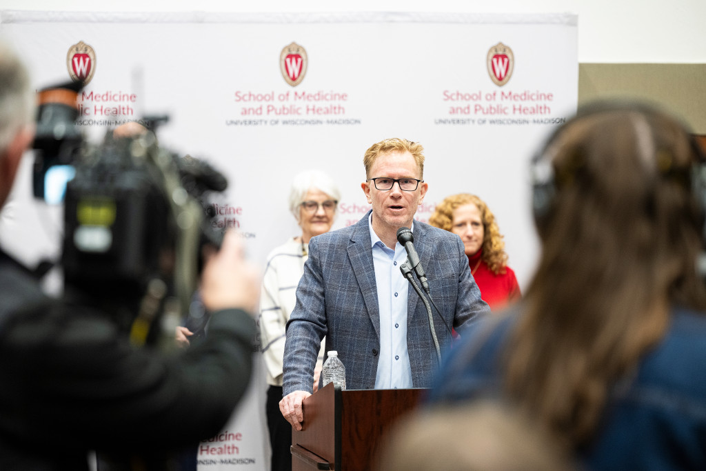 Johnson stands behind a podium and addresses a crowd of reporters. 