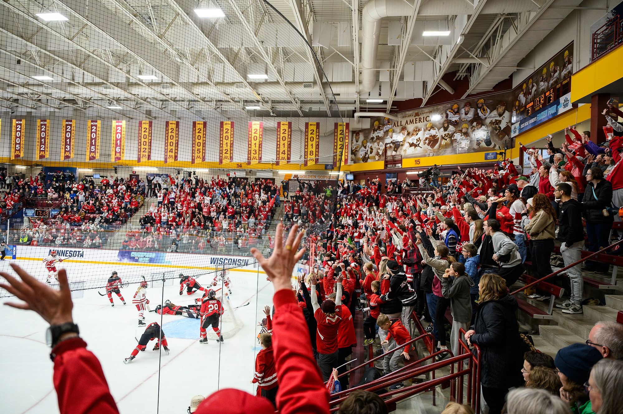 A large crowd throws their arms up in unison as the Badgers score a tying goal against the Ohio Buckeyes.