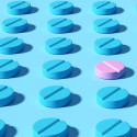 Illustration of rows of pill tablets, all in the color blue except for one in pink.
