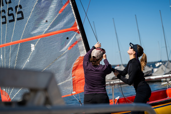 Two people lift a sail on a sailboat.