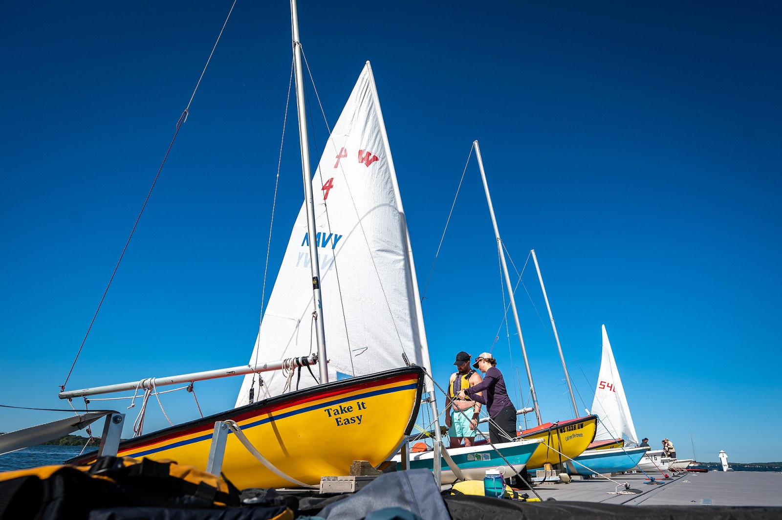 Two people tie some ropes on a sailboat.
