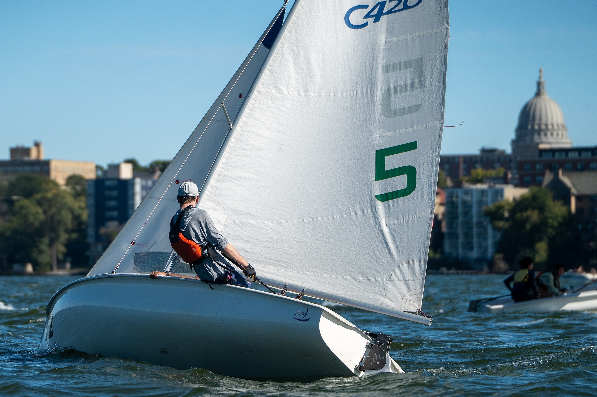 A person leans back on a boat sailing through the water. The state capitol is visible in the background.