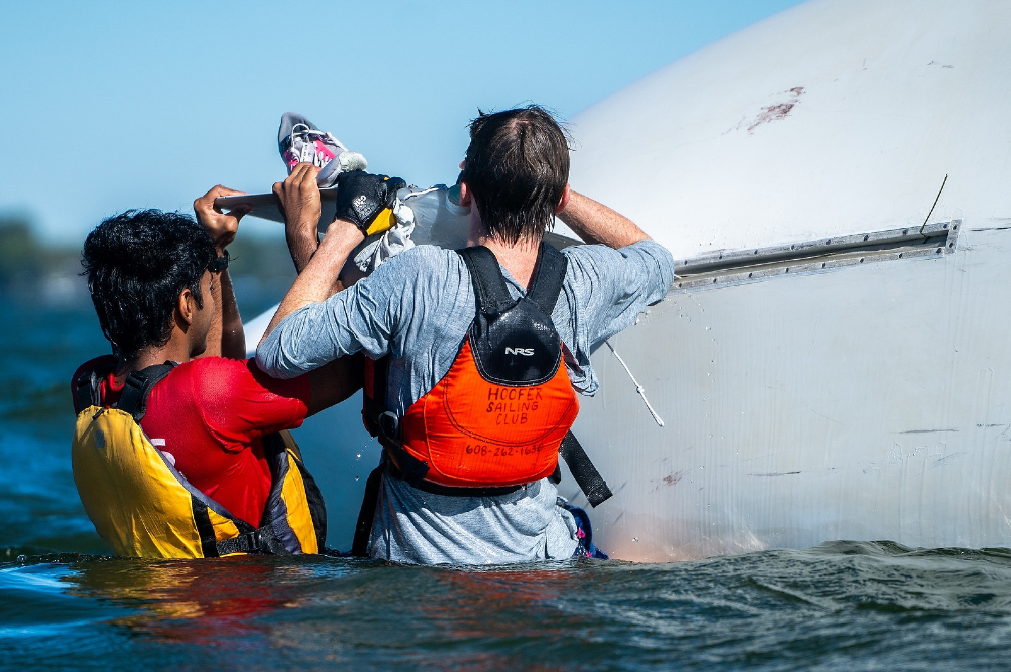 Two people work to set upright an overturned boat.