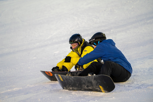 People crouch on a slope with a snowboard.