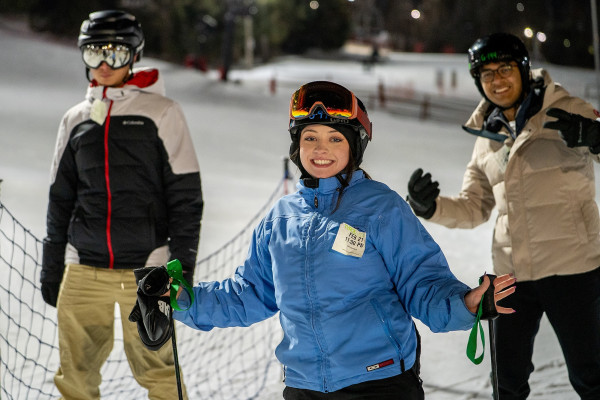 Three people wearing winter coats and ski helmets smile at the camera.