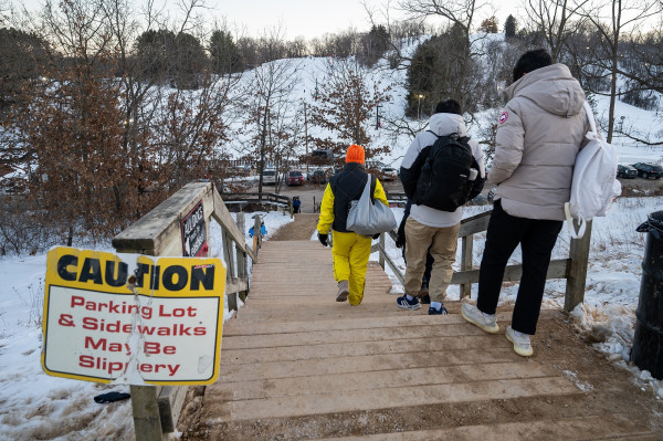 People walk toward a ski chalet carrying skis and snowboards.