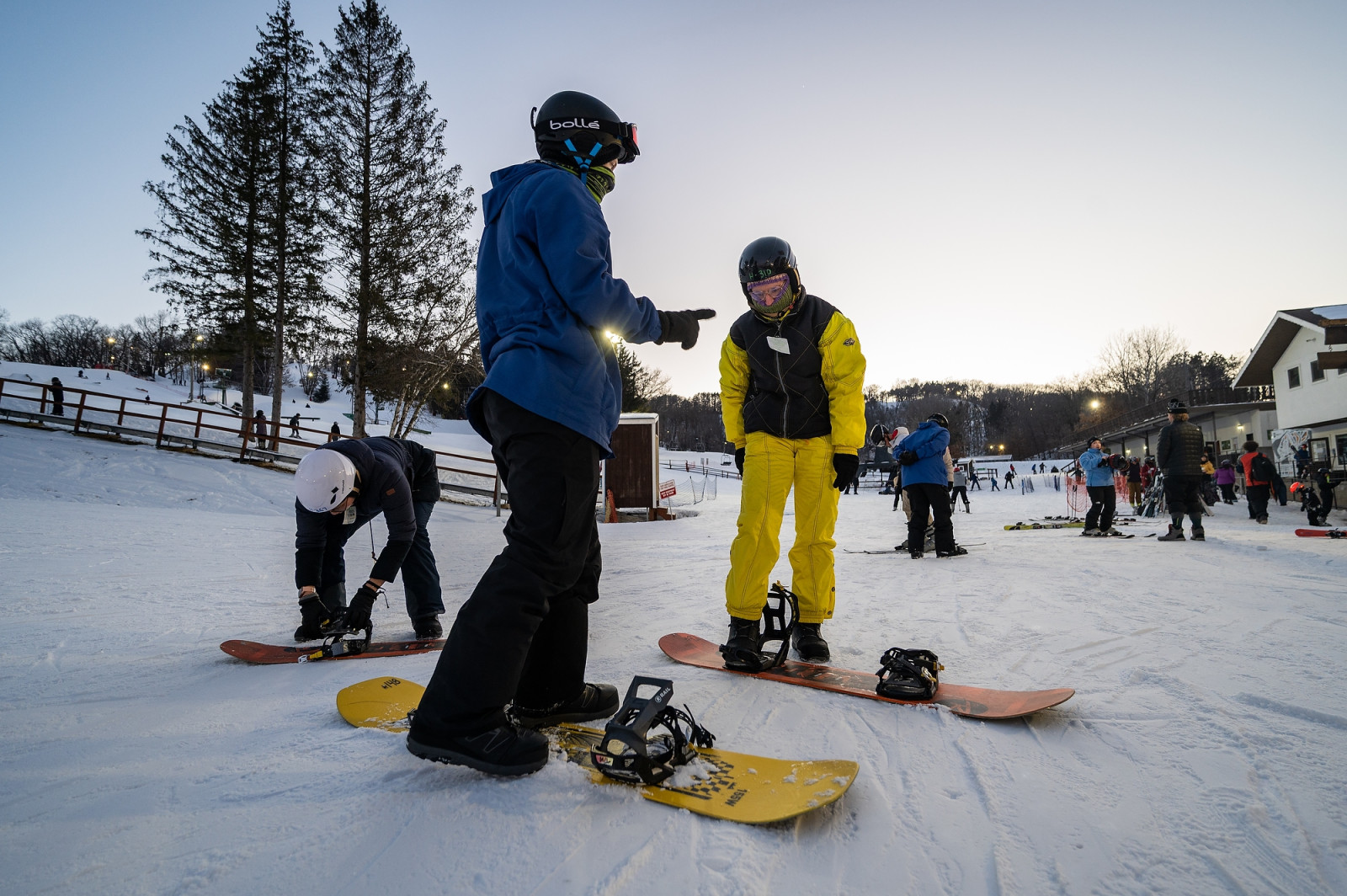 Two people stand on snowboards at the top of a slope.