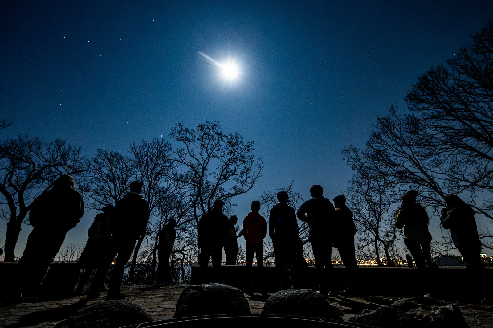 A group of people hike at night under a moon.
