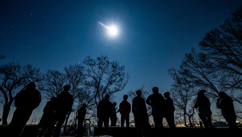 A group of people hike at night under a moon.