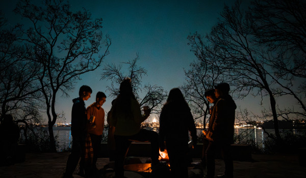 People gather around a bonfire at night.
