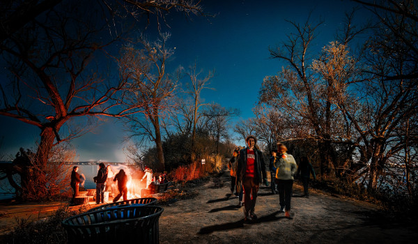 People walk in a night-time hike past a bonfire.