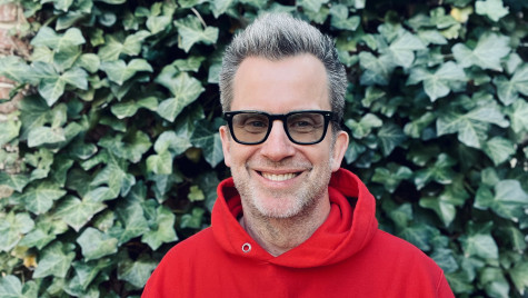 Jason Gay wears a red and white Wisconsin hoodie and smiles for a photo in front of an ivy-covered wall.