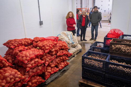Three people stand together in a modern dry storage facility. Piles of bagged potatoes lie on pallets.