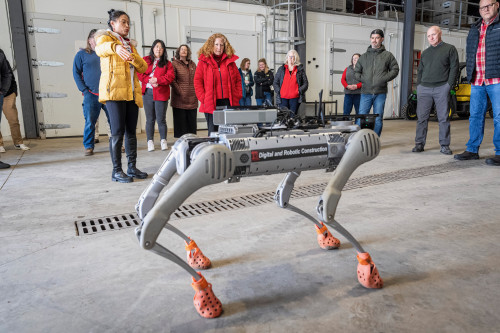 A person demonstrates the use of a robotic dog to a small crowd of onlookers.