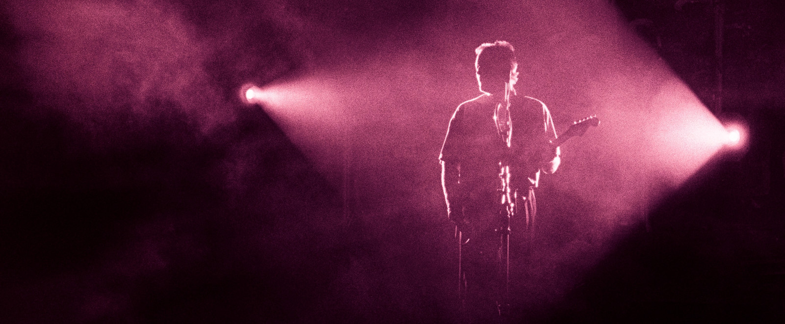 A guitar player in Pink Floyd stands on stage, with a spotlight shining on him.
